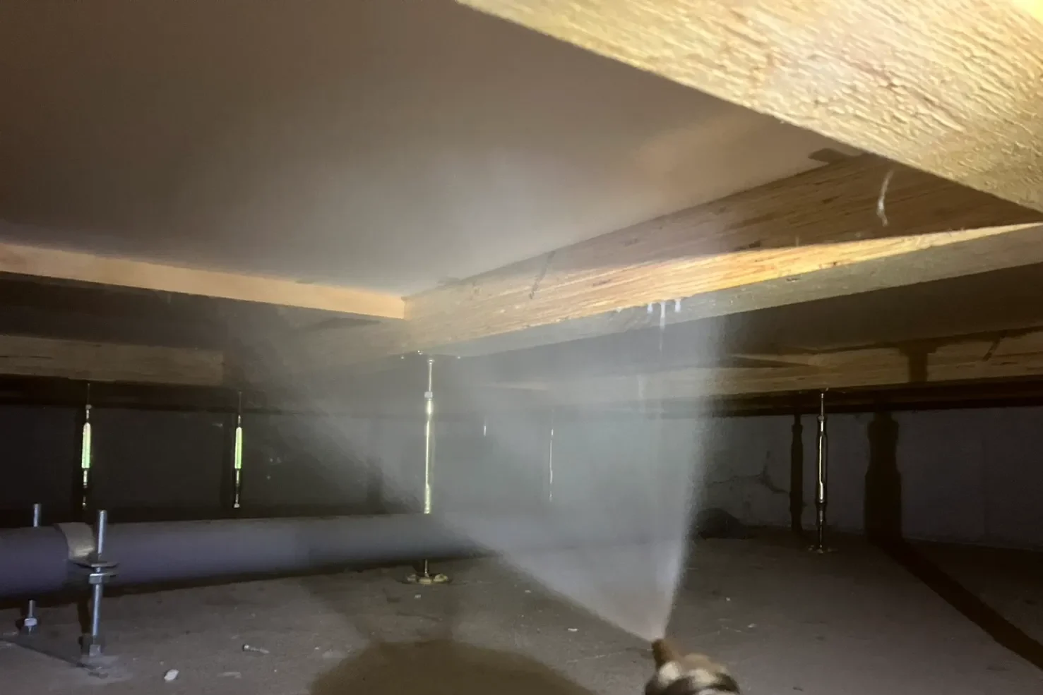 床下で噴霧器を使い、木材や基礎に白い霧状のシロアリ防除剤を散布する様子。