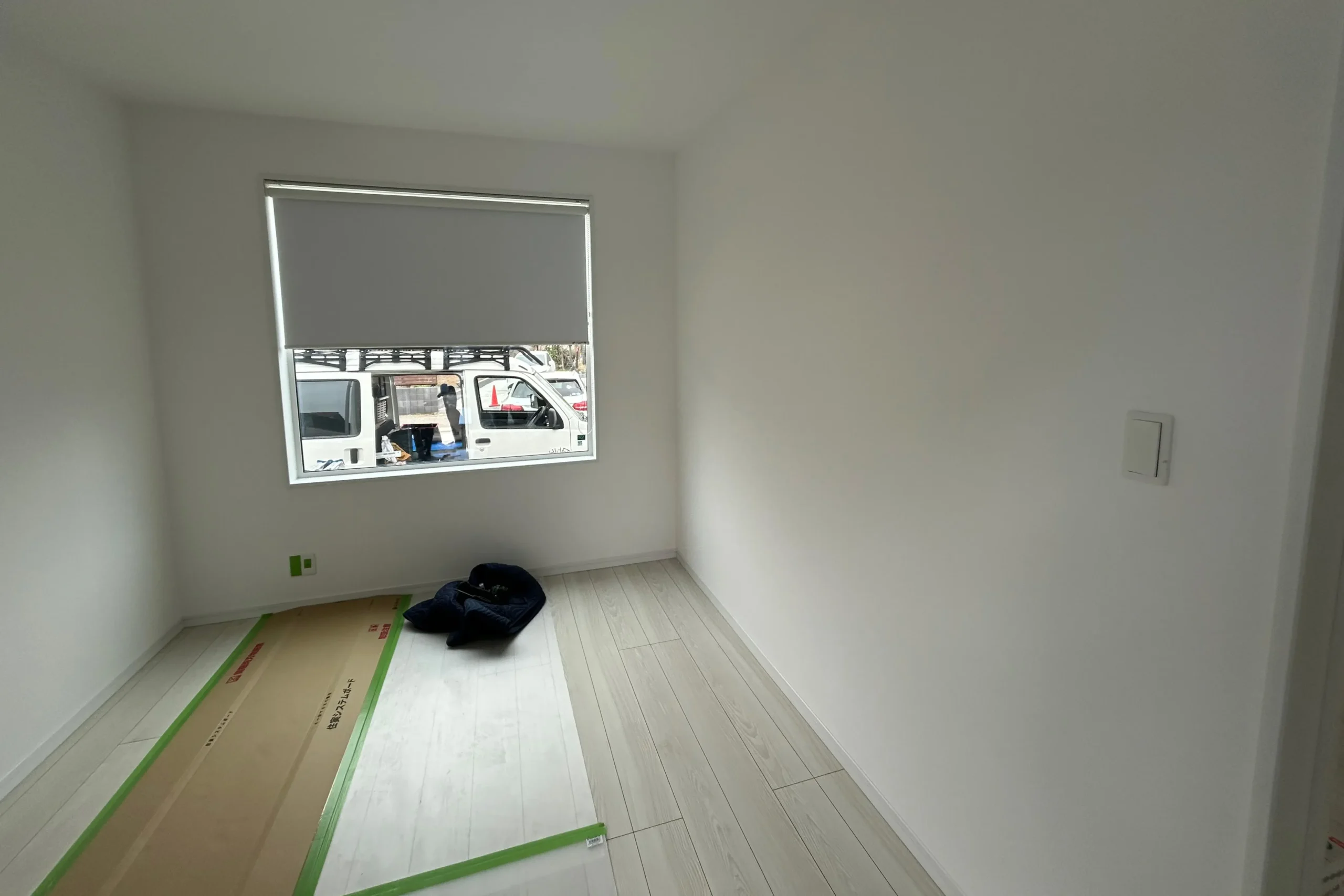 施工前の真っ白な壁と窓がある新築の個室。床には養生シートが敷かれている。