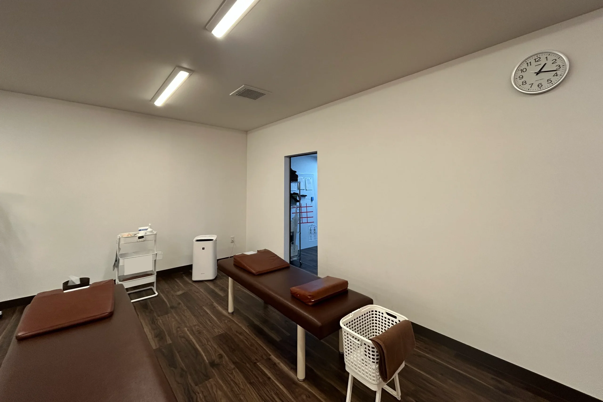整骨院の施術スペースの施工前。清潔感のあるダークブラウンの床と白い壁の広々とした室内。