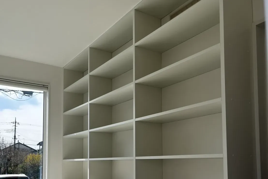 窓の右側に設置された、天井まで届く白い壁面収納棚。