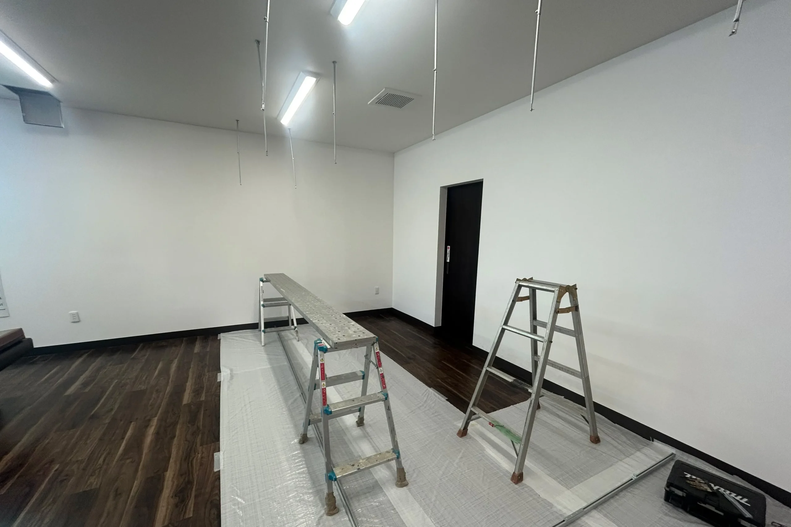 天井のカーテンレール取り付け作業。脚立と足場板を使い、床面を養生して慎重に下地を調査。