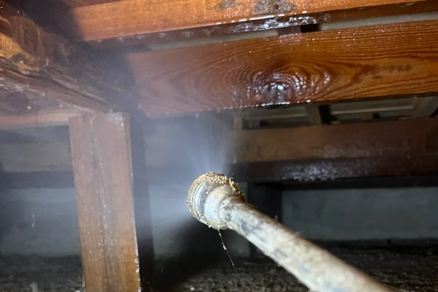 床下を支える床束（柱）と大引きの接合部に向けて、シロアリを駆除・予防するための薬剤を正確に散布している様子