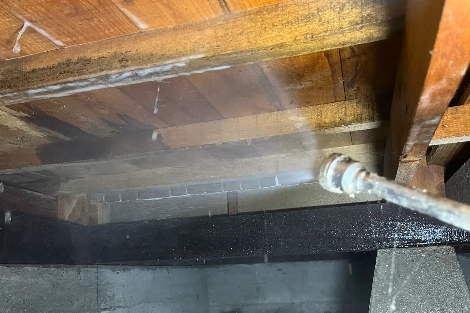  基礎が交差する隅の木部（土台や角の部分）に対して、シロアリの食害を防ぐための防蟻薬剤を丁寧に散布している様子