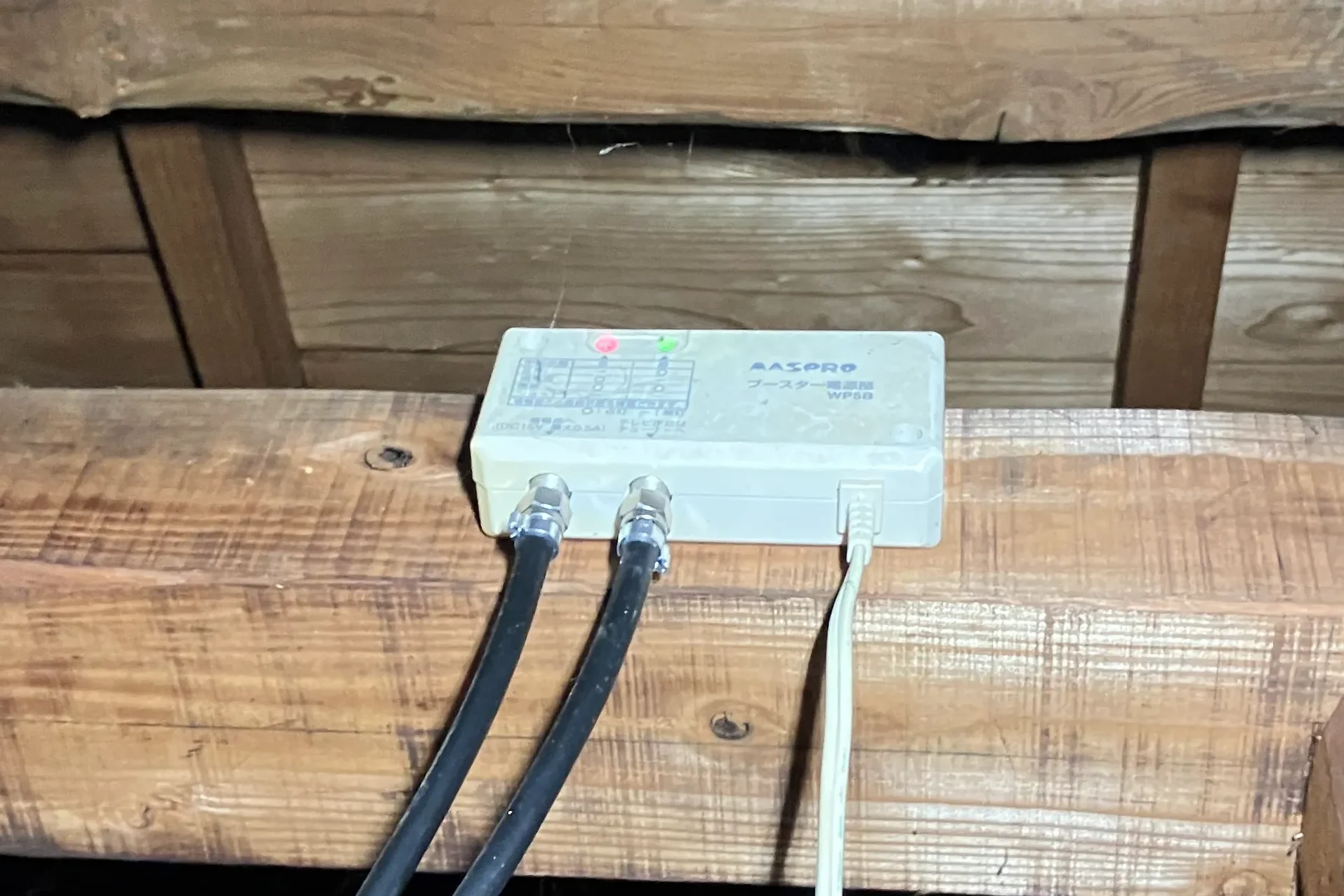 テレビが映らない原因を特定するため、屋根裏に設置されたブースター電源部の異常ランプを確認している様子