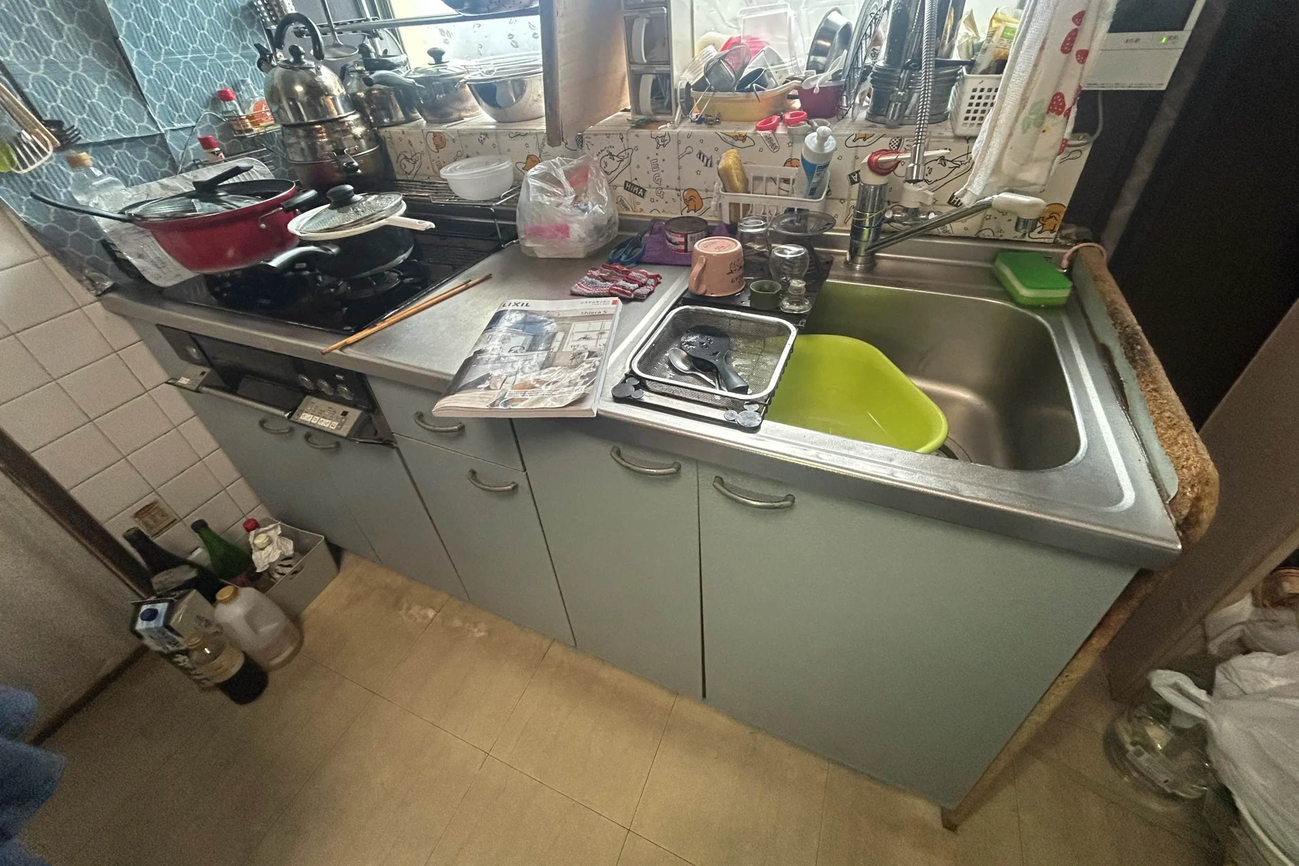  リフォーム前の古いキッチン。タイル壁と開き扉のシステムキッチンの様子。