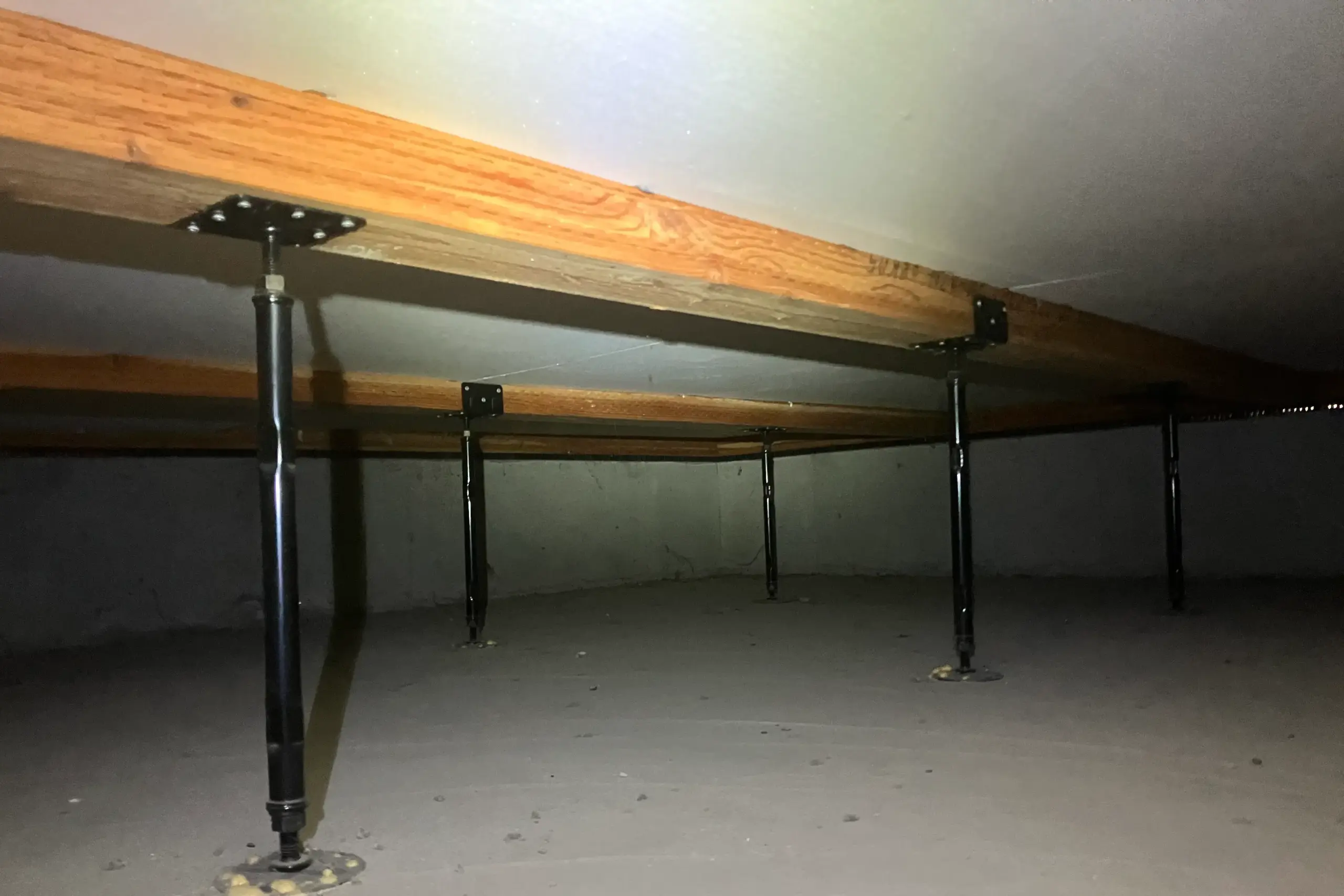 きれいな木材と黒い鋼製束（金属の支柱）が立つ、コンクリート（ベタ基礎）の床下の様子