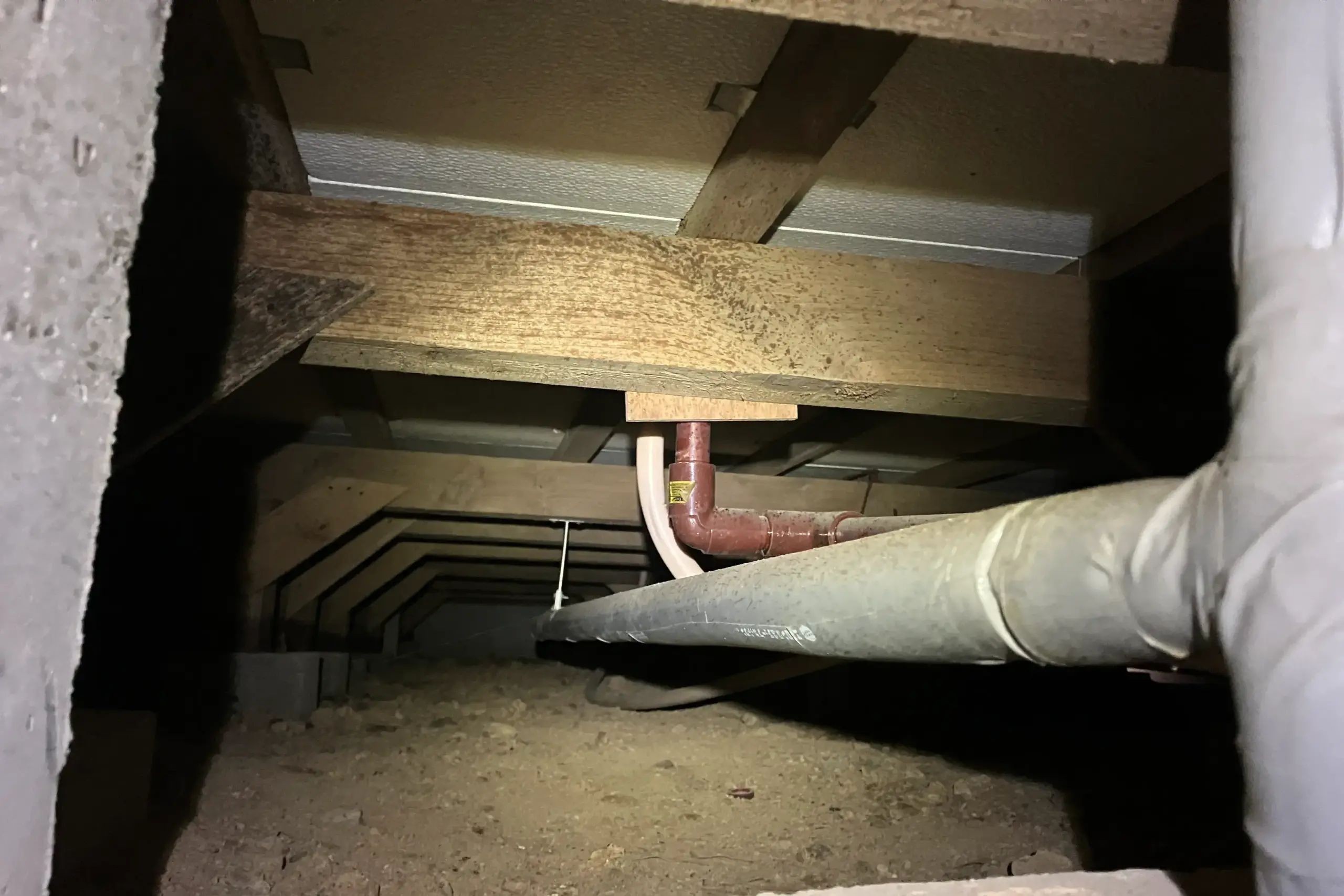 施工前の床下、土壌、配管、木材が見える