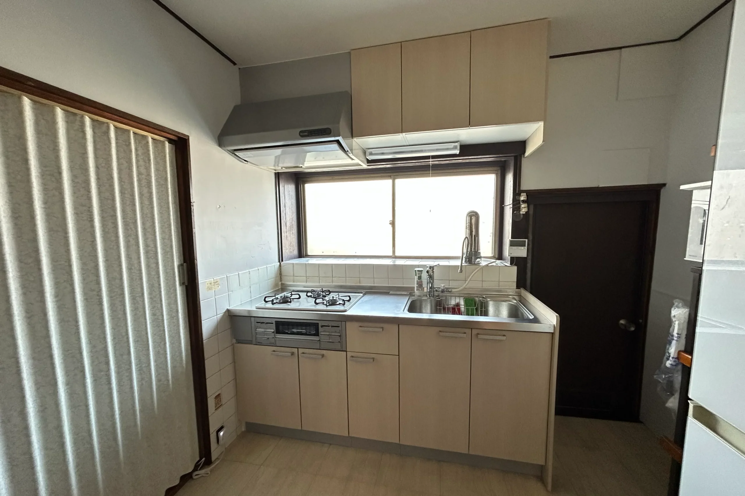  交換後の新しいシステムキッチン。木目調の扉と最新コンロを設置した完工写真。