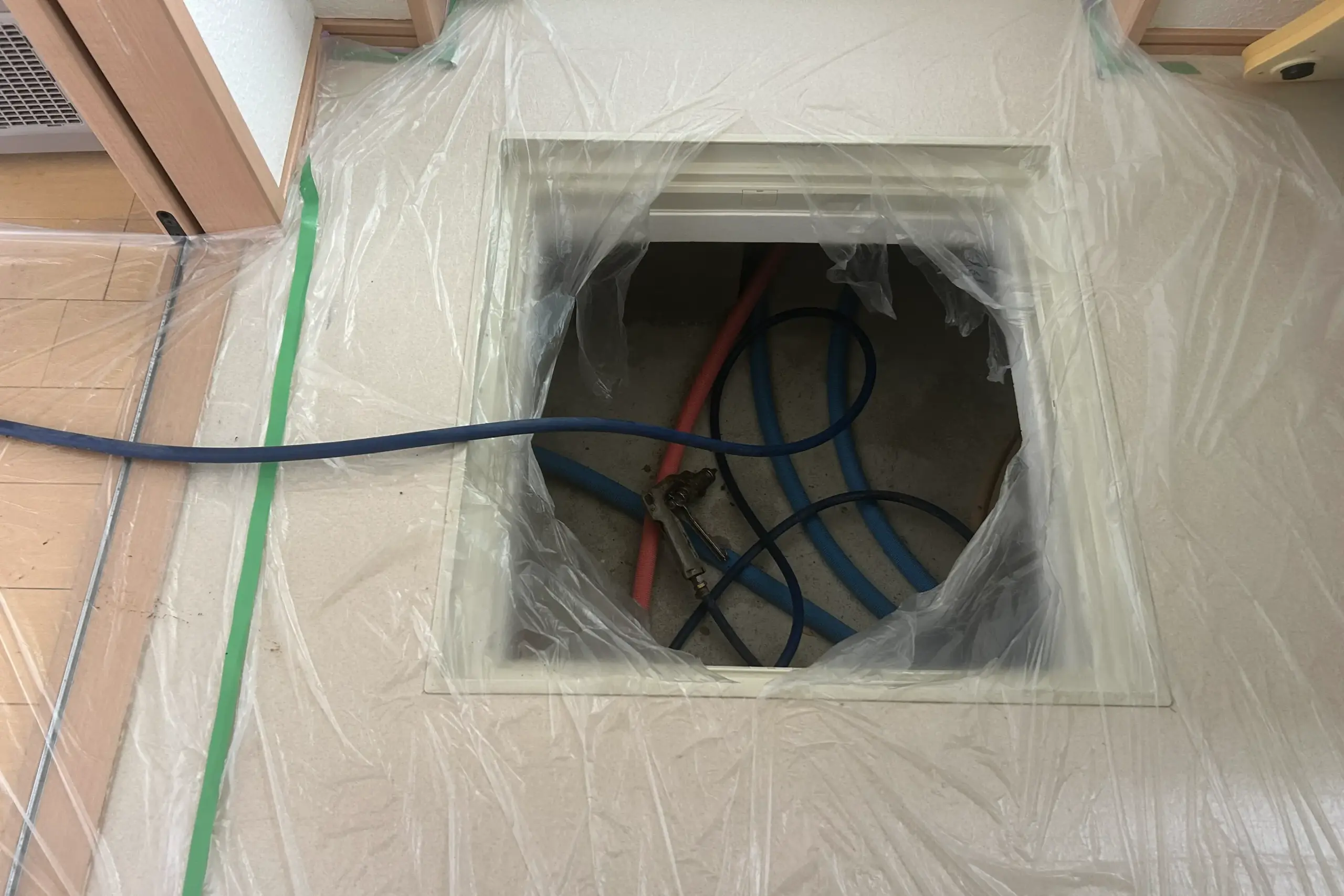 シロアリ予防・駆除の作業前の養生（ようじょう）作業。床下点検口の周辺をビニールシートで保護している様子