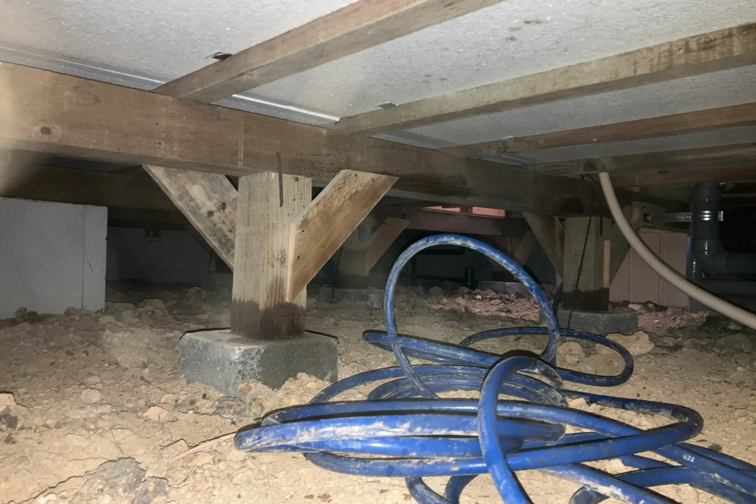 平屋の広い床下にシロアリ予防薬剤を散布するため、ロングホースを準備している様子